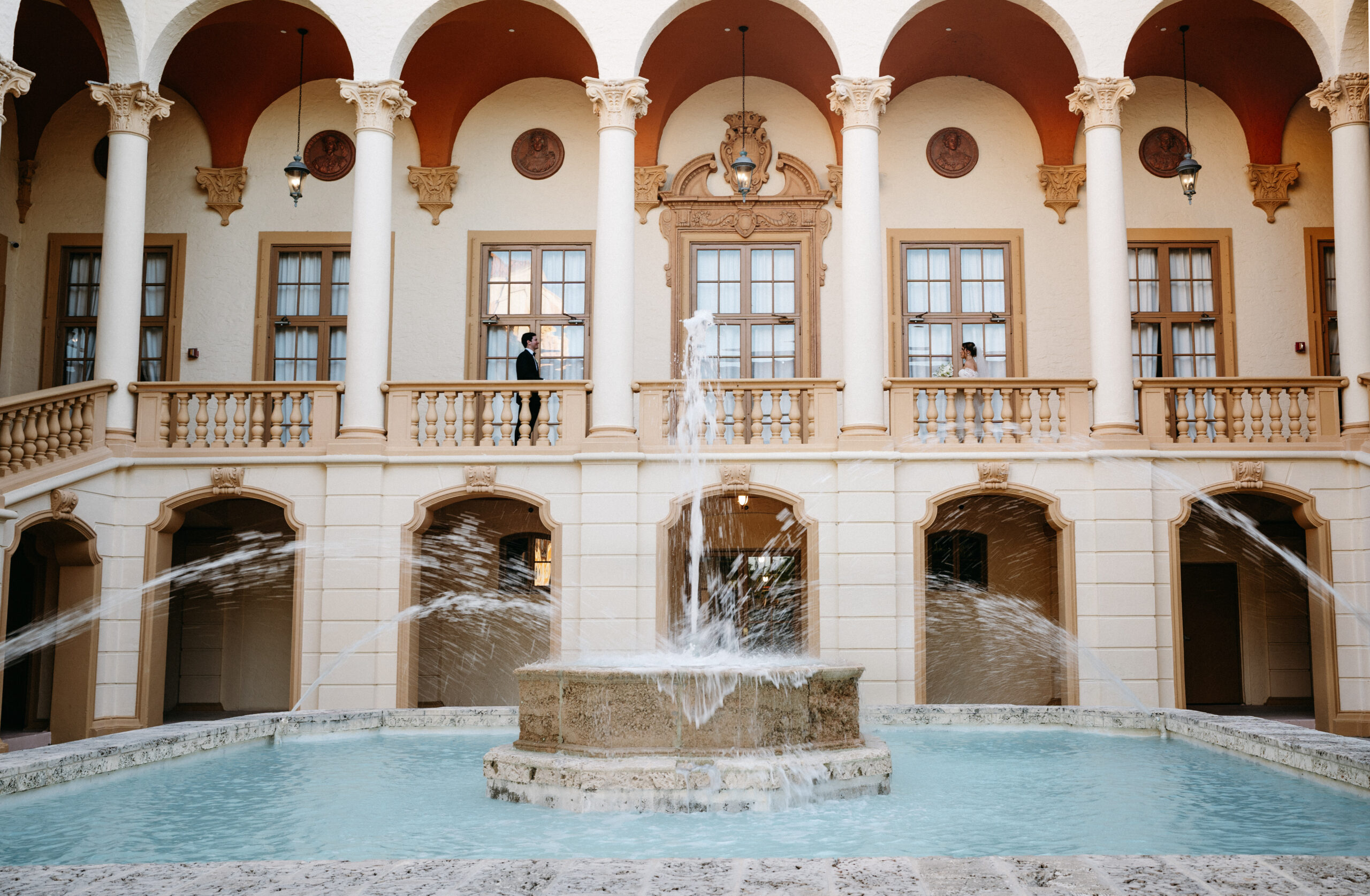 Couples bridal portraits on balcony overlooking iconic water fountain at Biltmore Hotel in Coral Gables.
